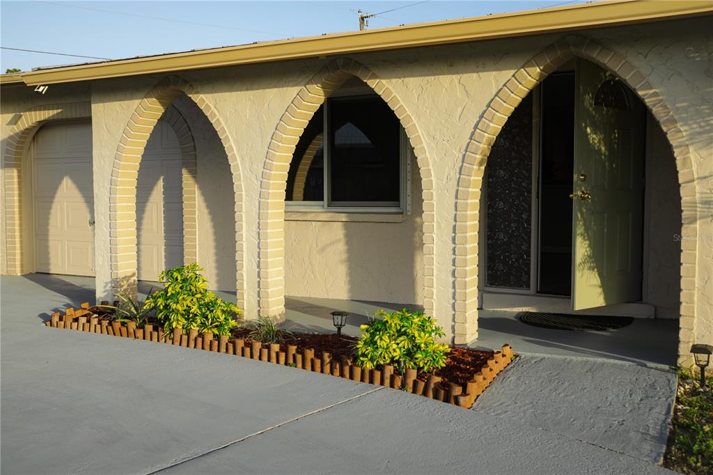 A house exterior featuring a concrete driveway, arched brick entryways, and a small garden bed — 389 MILLPORT STREET NW, PORT CHARLOTTE, FL