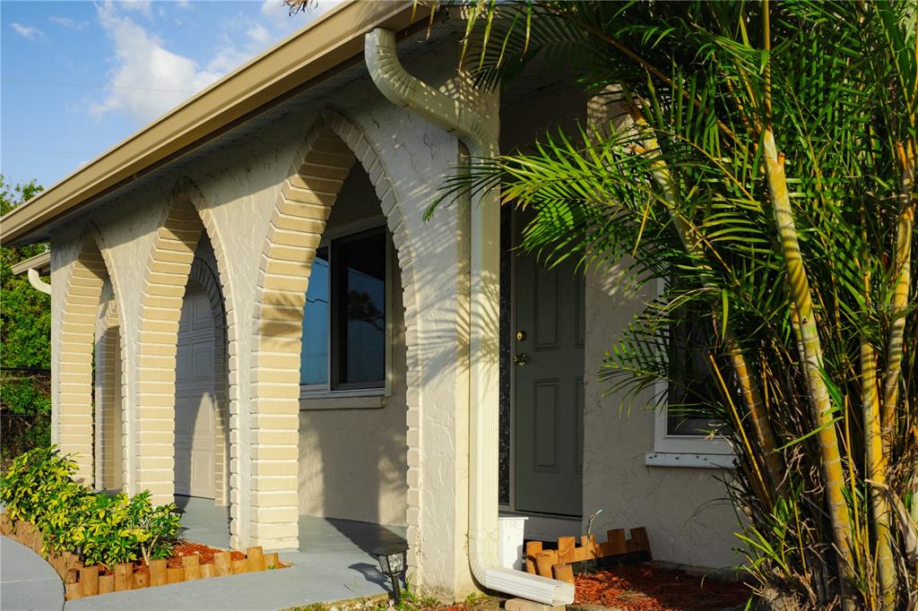 A house exterior features arched brick columns, a grey front door, and a palm tree — 389 MILLPORT STREET NW, PORT CHARLOTTE, FL