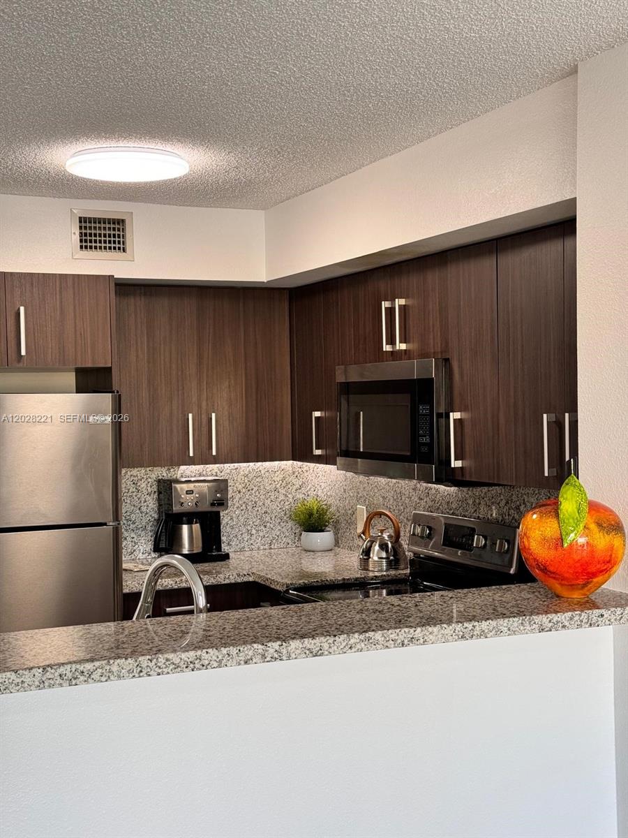 A kitchen features dark wood cabinets, granite countertops, stainless steel appliances, and a decorative apple — 4420 NW 107th Ave # 206, Doral FL 33178, DORAL, FL