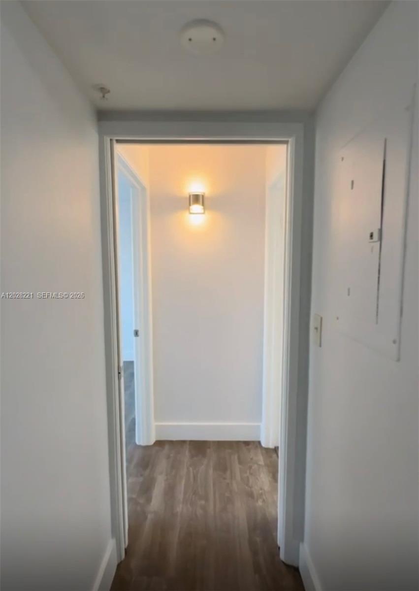 A narrow hallway with wood-look flooring leads to a doorway with a wall-mounted light fixture — 4420 NW 107th Ave # 206, Doral FL 33178, DORAL, FL