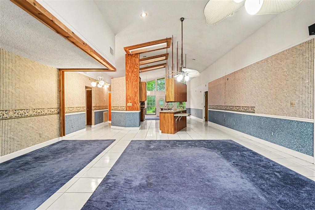 A spacious living area features blue carpeting, white tile flooring, wood accents, and wallpapered walls — 1235 MARSH FERN ROAD, MIMS, FL