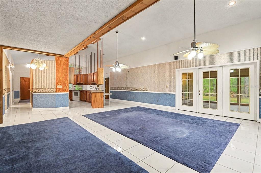 A large room with blue carpet, tiled floors, wood-paneled accents, and glass doors to outside — 1235 MARSH FERN ROAD, MIMS, FL