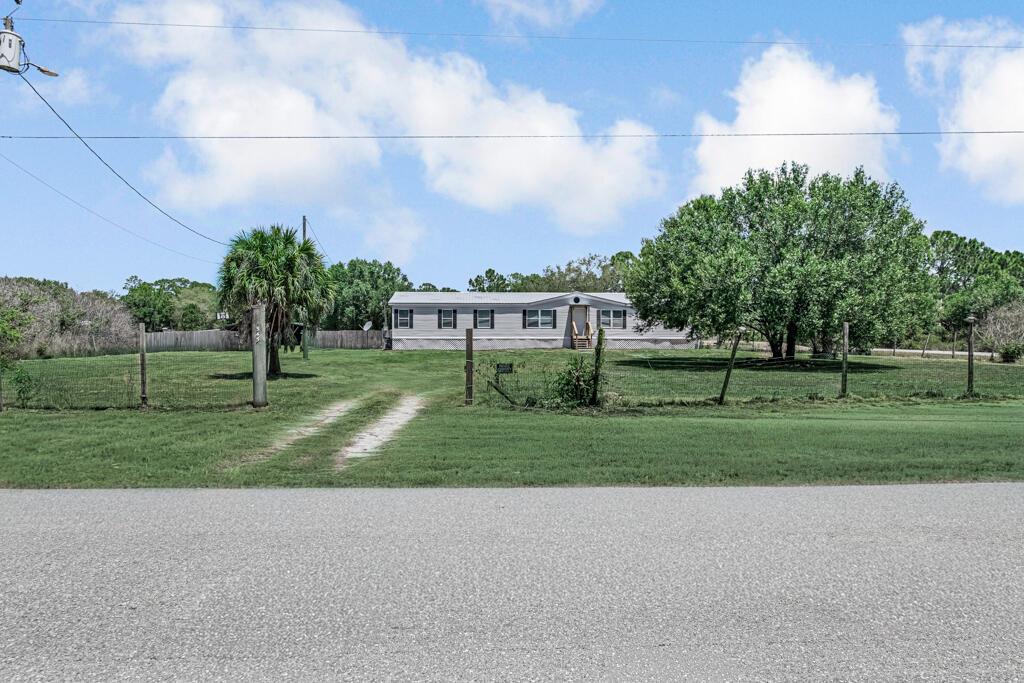A single-story manufactured home sits on a large, grassy lot behind a wire fence — 545 Bald Cypress Avenue, Clewiston FL 33440, CLEWISTON, FL