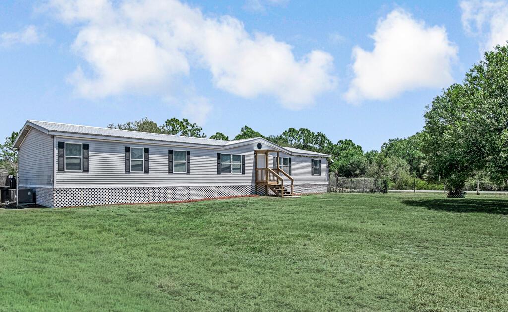 A single-story manufactured home with light gray siding sits on a large, grassy lot — 545 Bald Cypress Avenue, Clewiston FL 33440, CLEWISTON, FL