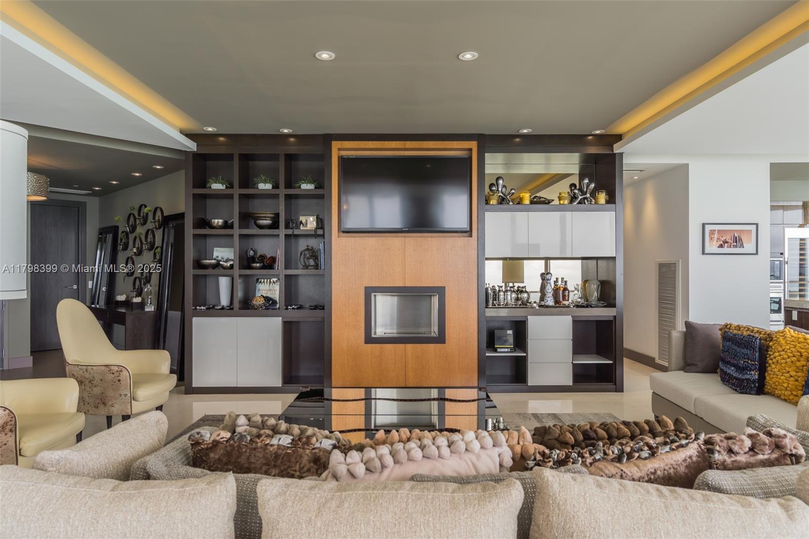 A living room features a central fireplace, a mounted television, and built-in shelving units — 9703 Collins Ave # 2100, Bal Harbour FL 33154, BAL HARBOUR, FL