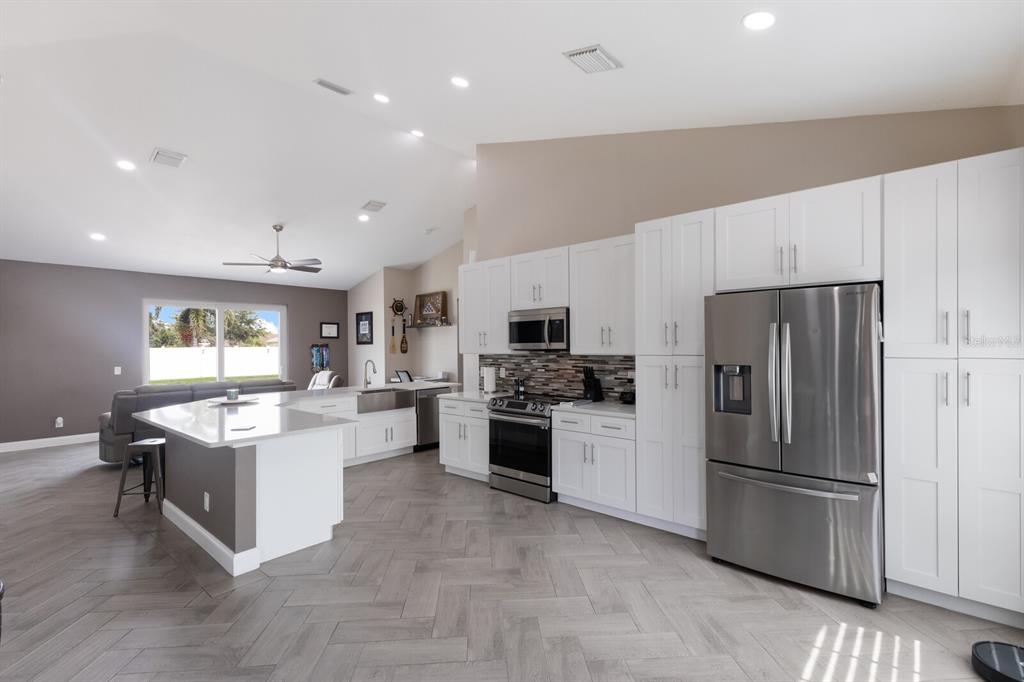 A modern kitchen with white cabinets, stainless steel appliances, and herringbone tile flooring — 1606 22ND AVENUE W, PALMETTO, FL
