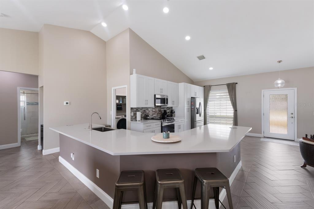 A kitchen with white cabinets, a quartz island, and bar stools overlooks a living area — 1606 22ND AVENUE W, PALMETTO, FL