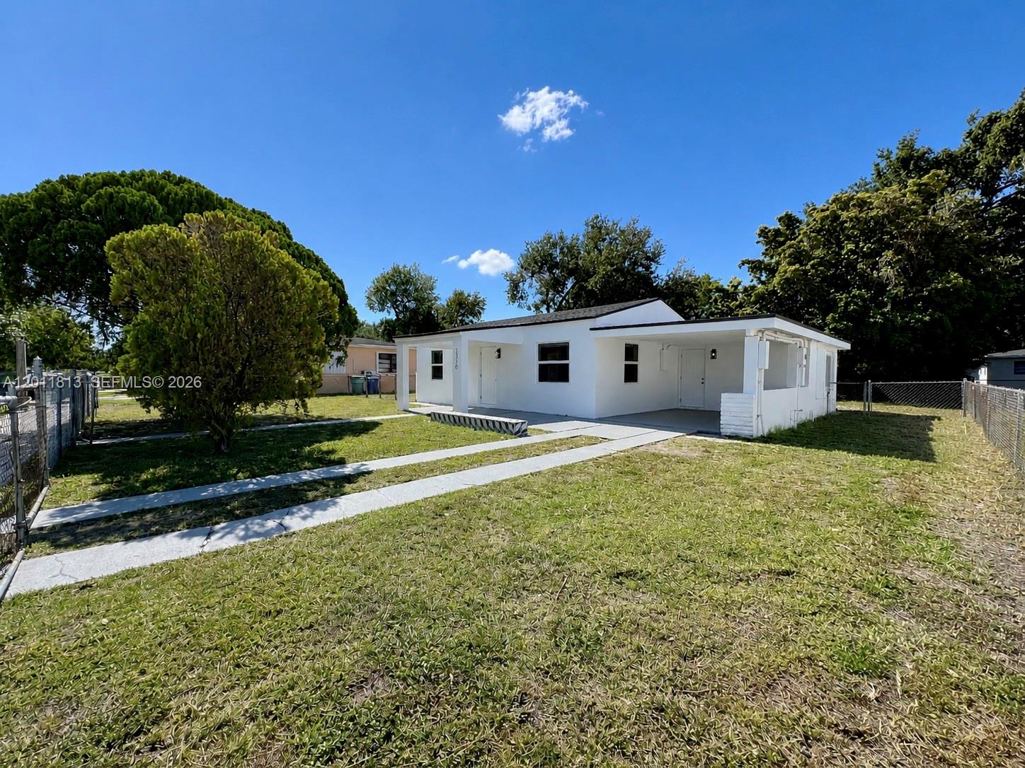 A white single-story house with a carport sits on a grassy lot under a blue sky — 2370 NW 96th St, Miami FL 33147, MIAMI, FL