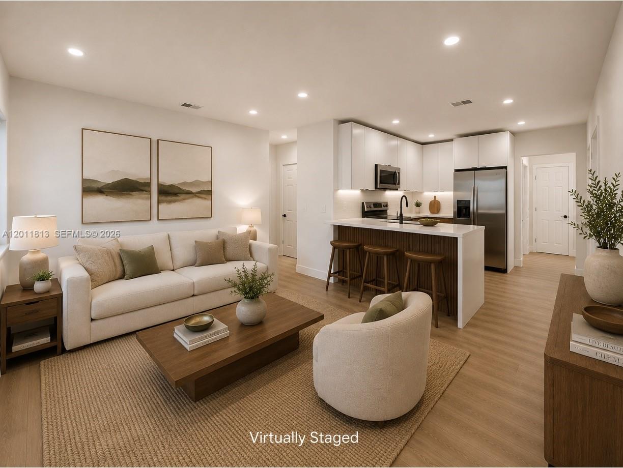 This virtually staged living room features a kitchen island, white cabinetry, and light wood flooring — 2370 NW 96th St, Miami FL 33147, MIAMI, FL