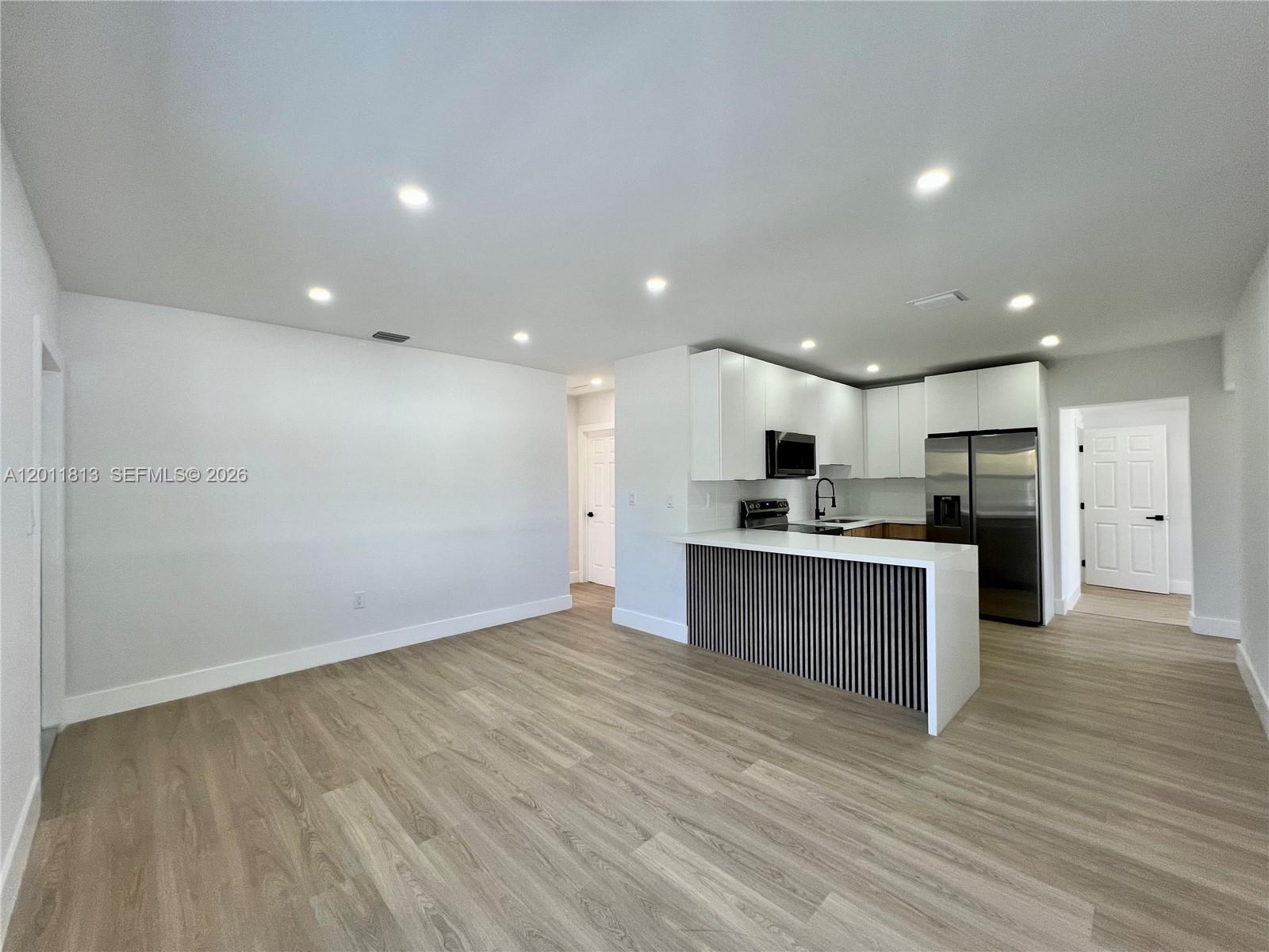 A modern kitchen features white cabinetry, stainless steel appliances, and a slatted breakfast bar island — 2370 NW 96th St, Miami FL 33147, MIAMI, FL