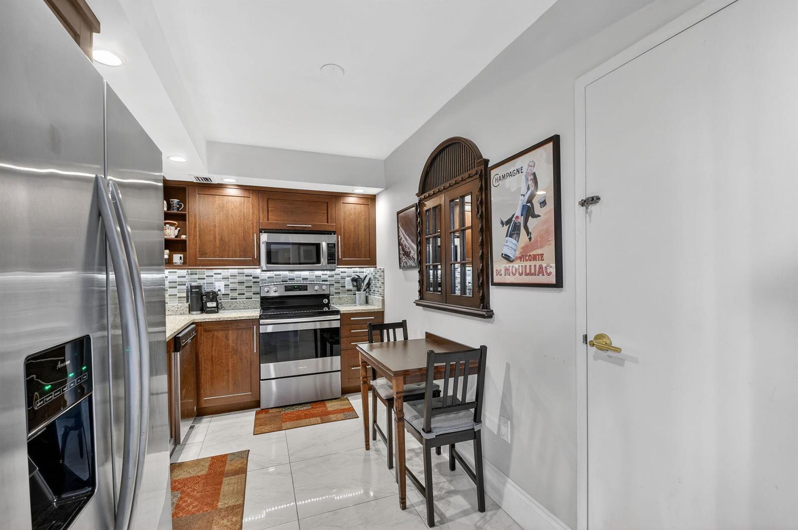 A kitchen with stainless steel appliances, wood cabinets, tiled floors, and a small dining set — 3450 S Ocean Boulevard # 423, Palm Beach FL 33480, PALM BEACH, FL