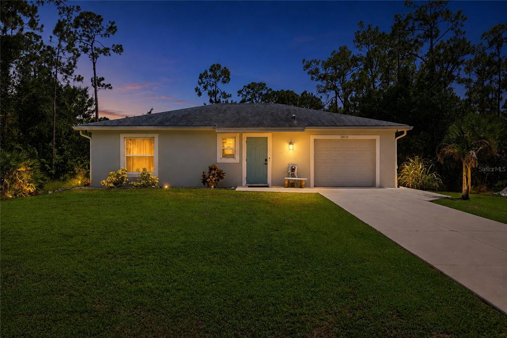 A single-story house with a light-colored exterior, a garage, and a front lawn at dusk — 28111 MANFRED DRIVE, PUNTA GORDA, FL
