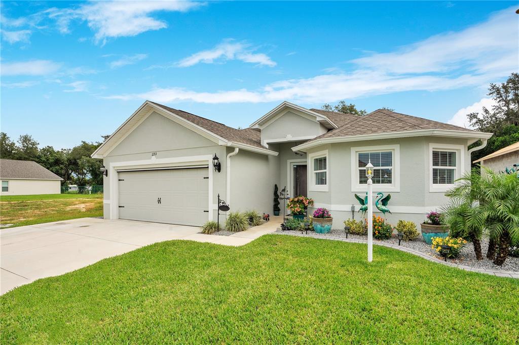 A single-story house with a light green exterior, a two-car garage, and a landscaped yard — 1153 BISHOP STREET, AVON PARK, FL