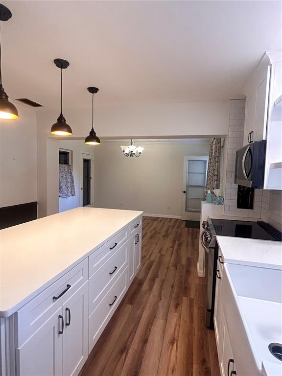 A kitchen with white cabinets, a large island, and wood-look flooring leads to a dining area — 2009 POE STREET, LAKELAND, FL