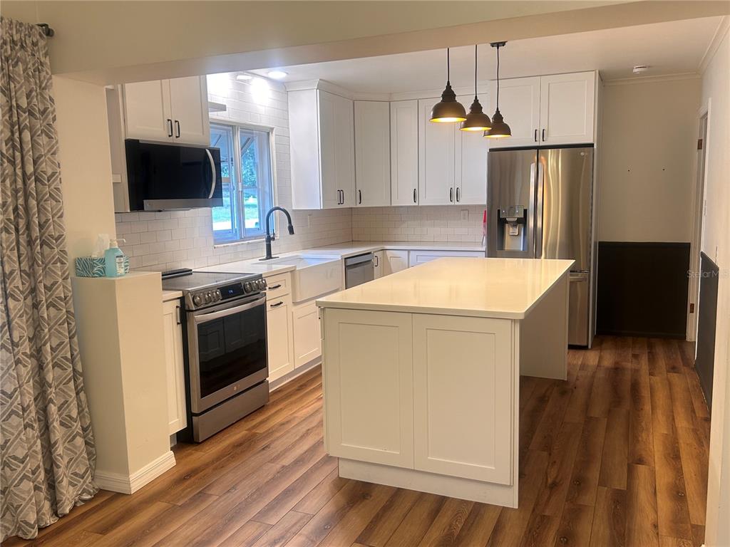 A kitchen with white cabinets, stainless steel appliances, a center island, and wood-look flooring — 2009 POE STREET, LAKELAND, FL