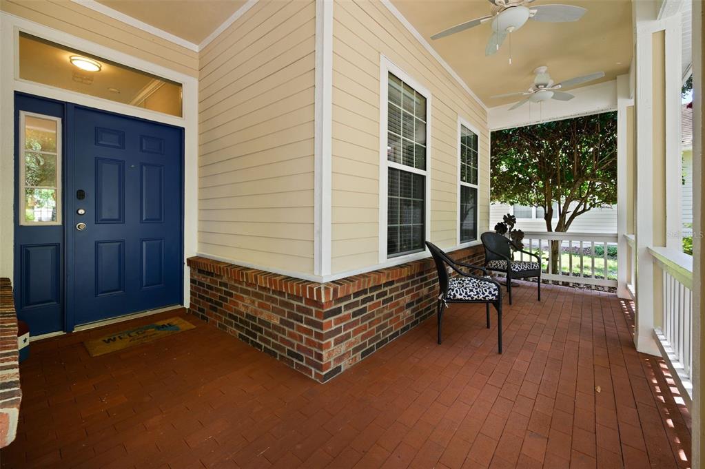 A covered front porch features a blue door, brick flooring, and two outdoor chairs — 9044 SW 25TH ROAD, GAINESVILLE, FL