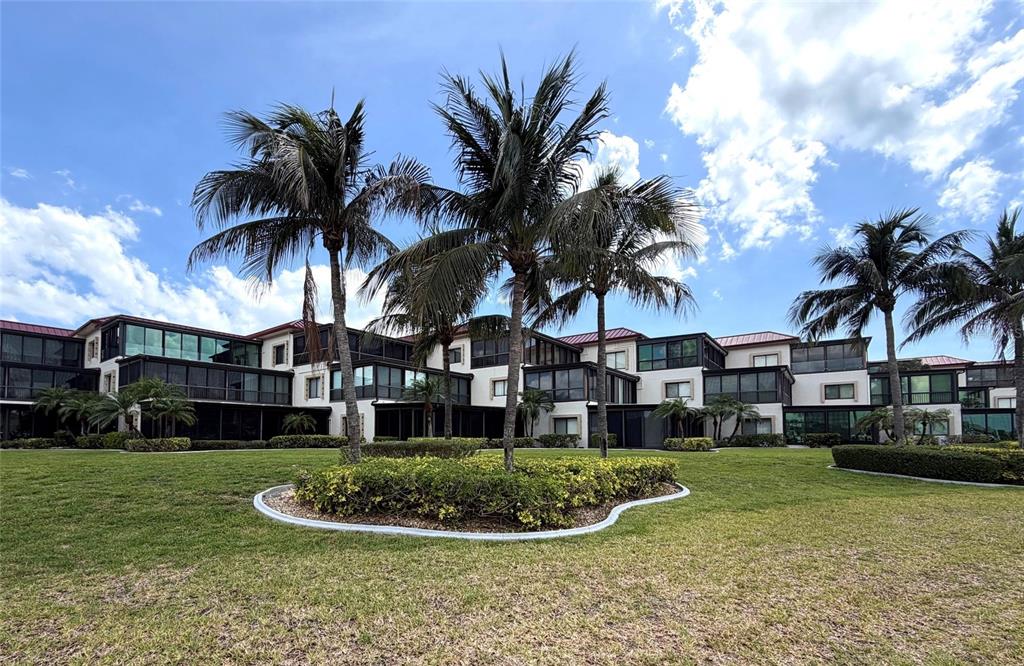 A multi-story residential building with screened balconies sits behind a manicured lawn and palm trees — 3230 SOUTHSHORE DRIVE UNIT 34A, PUNTA GORDA, FL