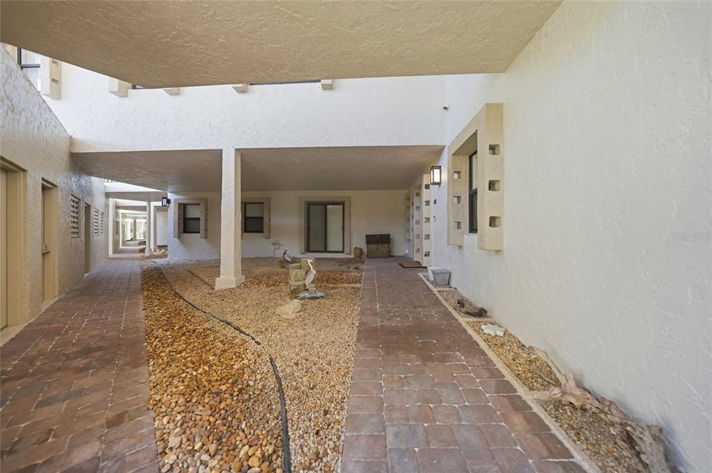 A covered outdoor walkway with paver paths and a gravel garden area between building walls — 3230 SOUTHSHORE DRIVE UNIT 34A, PUNTA GORDA, FL