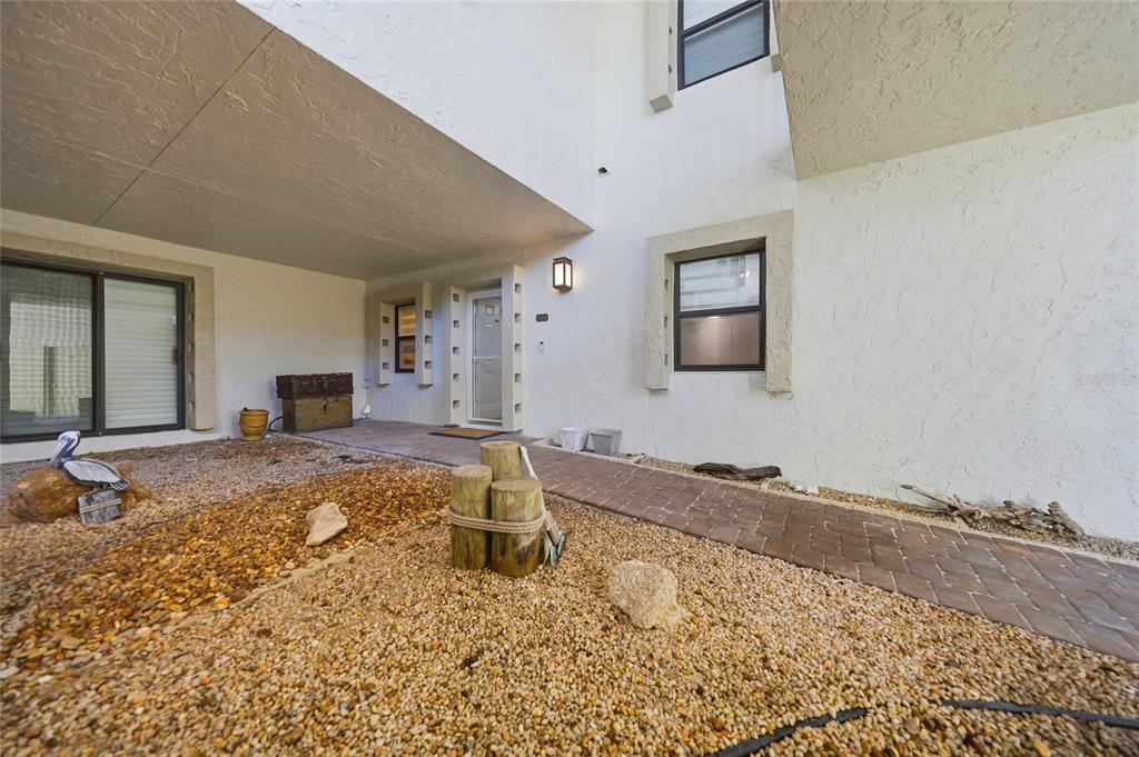 A covered entryway features a brick walkway, gravel landscaping, and a white stucco exterior — 3230 SOUTHSHORE DRIVE UNIT 34A, PUNTA GORDA, FL