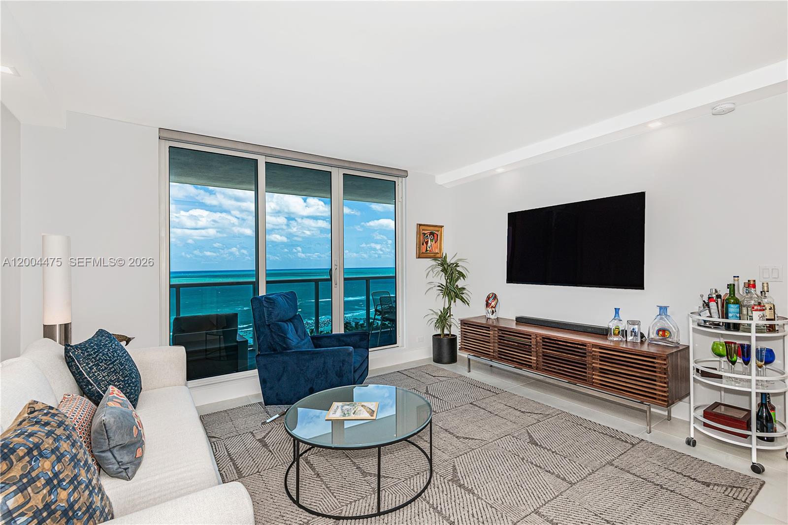 A living room features a white sofa, blue armchair, glass coffee table, and ocean views — 2301 Collins Ave # 1440, Miami Beach FL 33139, MIAMI BEACH, FL