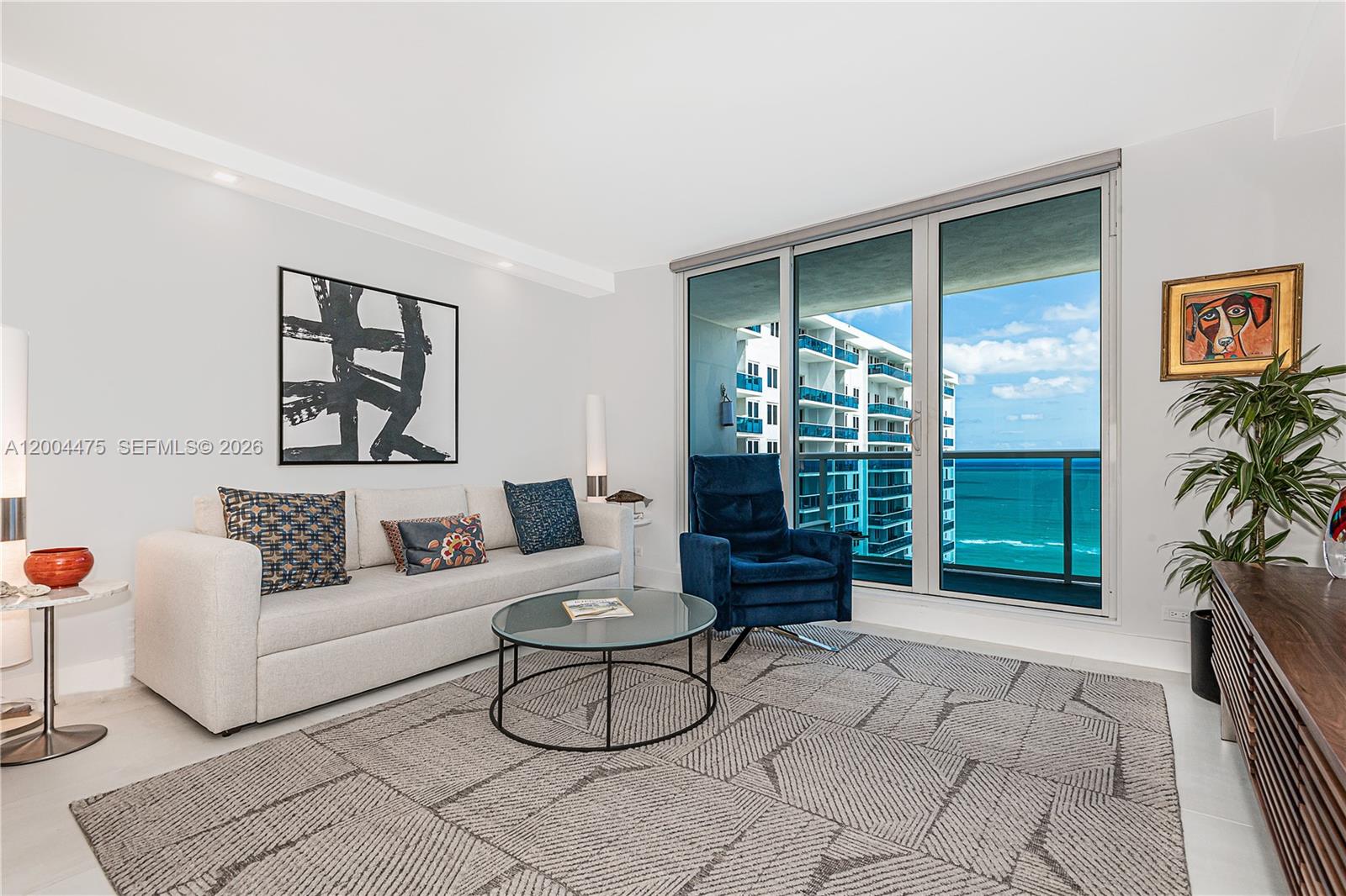 A living room features a light sofa, blue armchair, glass coffee table, and ocean views — 2301 Collins Ave # 1440, Miami Beach FL 33139, MIAMI BEACH, FL