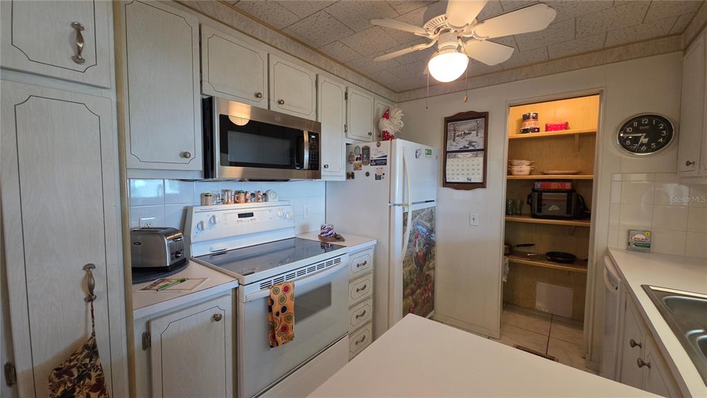 A kitchen features white cabinetry, stainless steel appliances, a ceiling fan, and an open pantry — 5406 BALI COURT, BRADENTON, FL