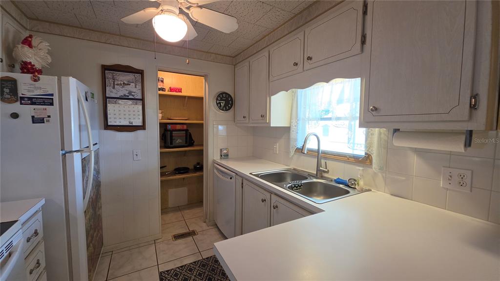 A kitchen features white cabinets, a double-basin sink, a refrigerator, and an adjacent pantry — 5406 BALI COURT, BRADENTON, FL