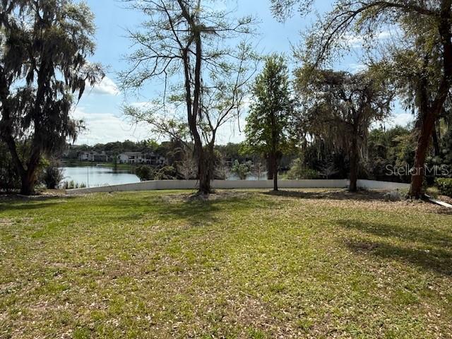 A grassy backyard features mature trees and a white fence overlooking a lake — 610 JASMINE ROAD, ALTAMONTE SPRINGS, FL
