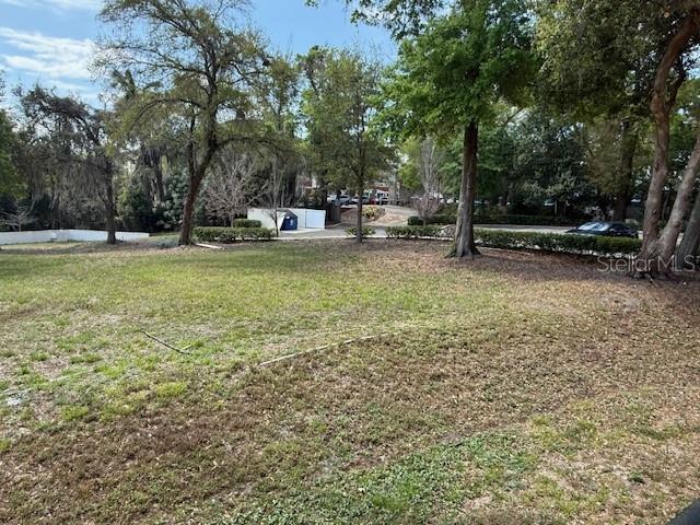 A grassy, sloped lot features scattered trees and a distant view of a parking area — 610 JASMINE ROAD, ALTAMONTE SPRINGS, FL