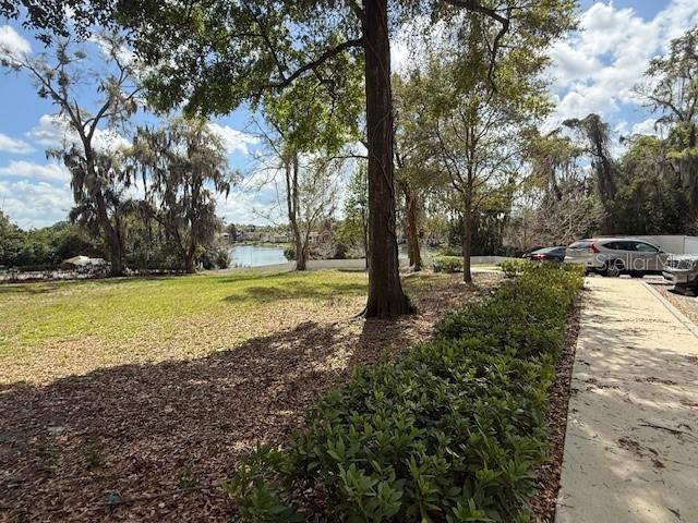 A grassy yard with trees and a sidewalk leads toward a distant lake — 610 JASMINE ROAD, ALTAMONTE SPRINGS, FL