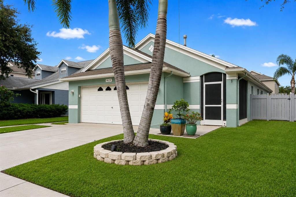 A light green single-story house features a two-car garage, palm trees, and a screened entryway — 8620 PERSEA COURT, NEW PORT RICHEY, FL