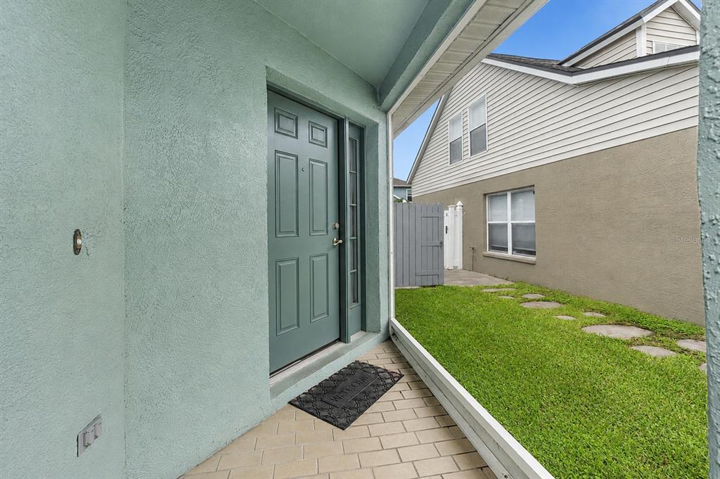 A covered entryway with a teal front door, a welcome mat, and a side yard — 8620 PERSEA COURT, NEW PORT RICHEY, FL