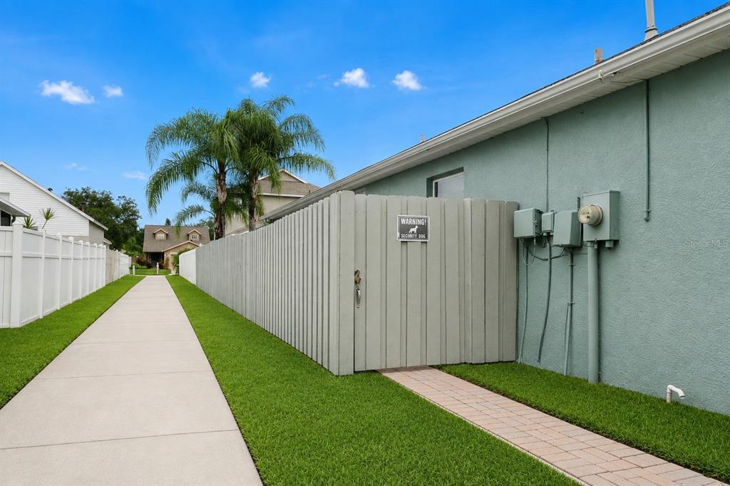 A concrete walkway runs between a white fence and a house with a wooden gate — 8620 PERSEA COURT, NEW PORT RICHEY, FL
