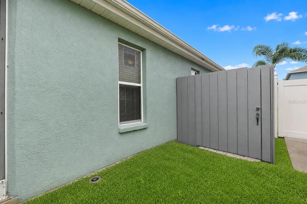 A light green stucco exterior wall with a window and a grey privacy fence — 8620 PERSEA COURT, NEW PORT RICHEY, FL