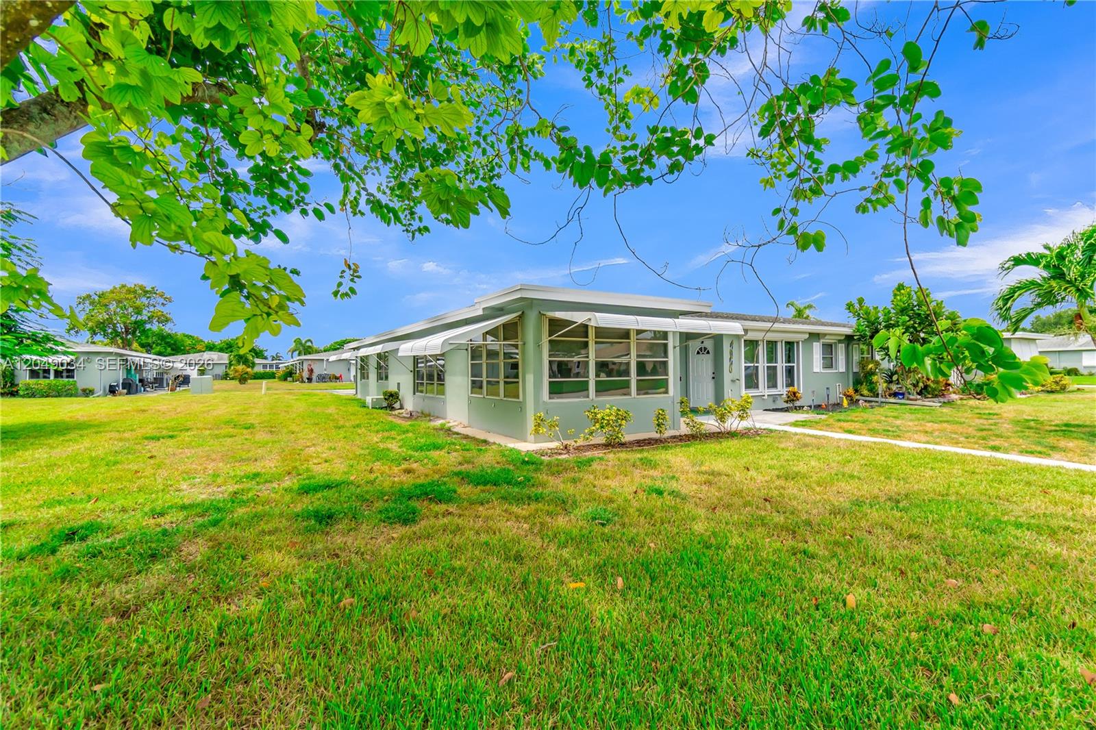 A single-story light green house with white awnings sits on a large grassy lot — 775 North Dr # A, Delray Beach FL 33445, DELRAY BEACH, FL
