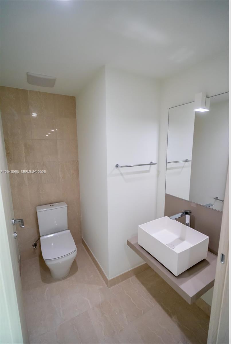 A modern bathroom features a white vessel sink, a wall-mounted vanity, and beige tiled walls — 1000 Brickell Plaza # 2506, Miami FL 33131, MIAMI, FL