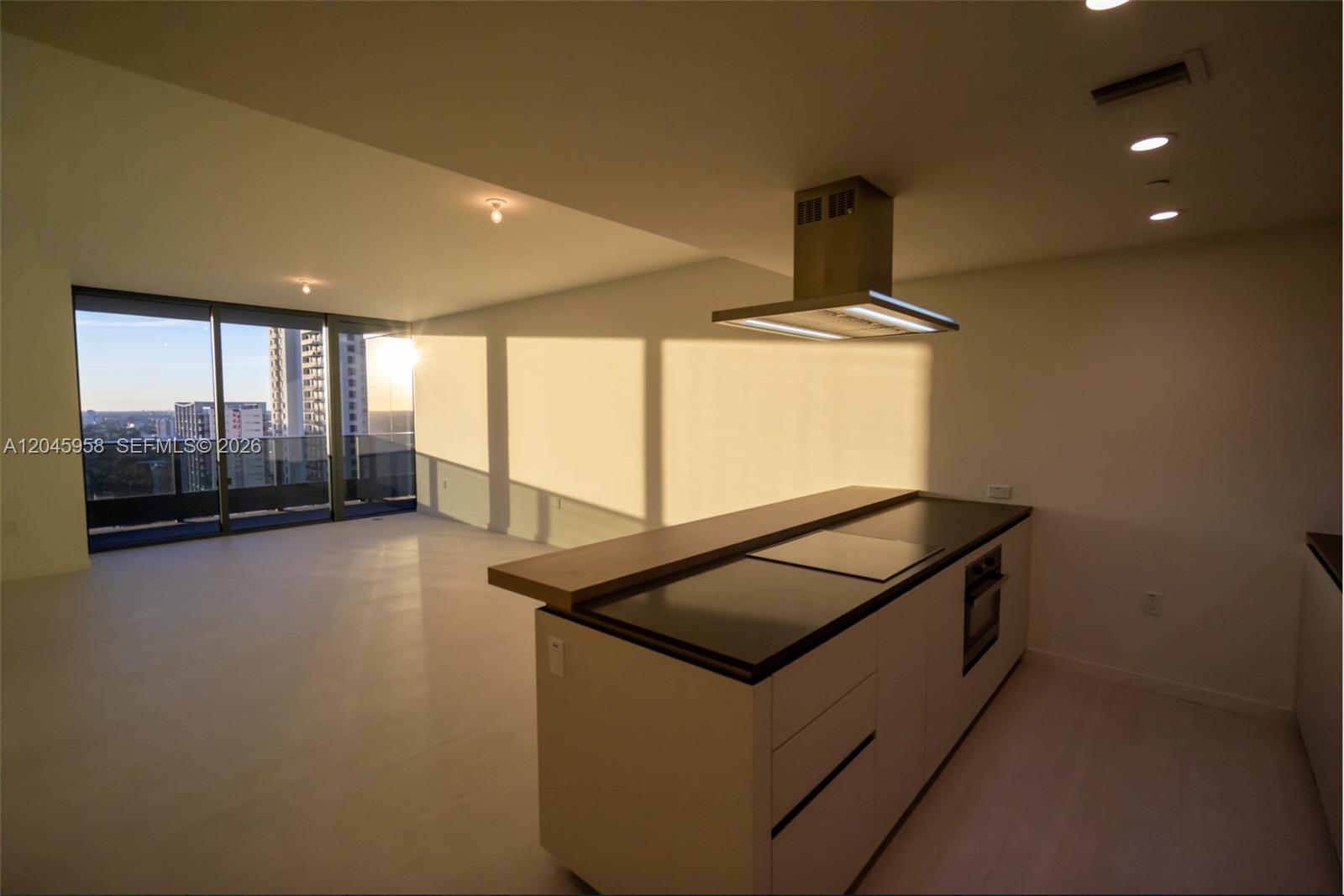 A modern kitchen island with a range hood sits in an open-plan apartment with floor-to-ceiling windows — 1000 Brickell Plaza # 2506, Miami FL 33131, MIAMI, FL