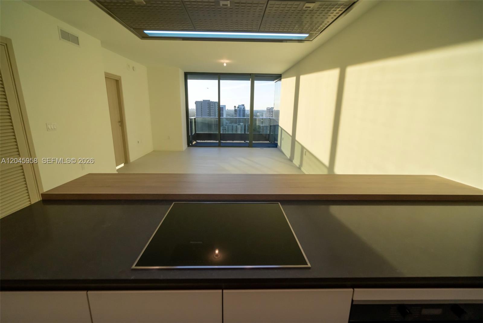 A kitchen island with a black cooktop overlooks an empty living area with balcony access — 1000 Brickell Plaza # 2506, Miami FL 33131, MIAMI, FL