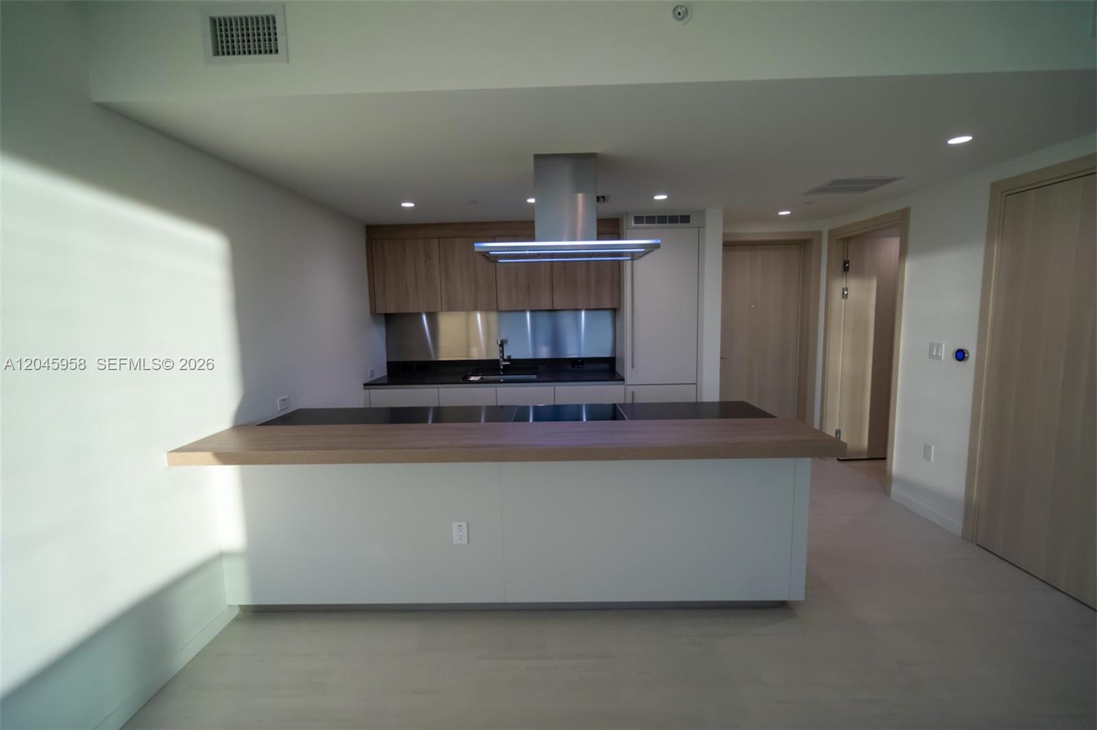 A modern kitchen features a wooden island, stainless steel range hood, and light wood cabinetry — 1000 Brickell Plaza # 2506, Miami FL 33131, MIAMI, FL
