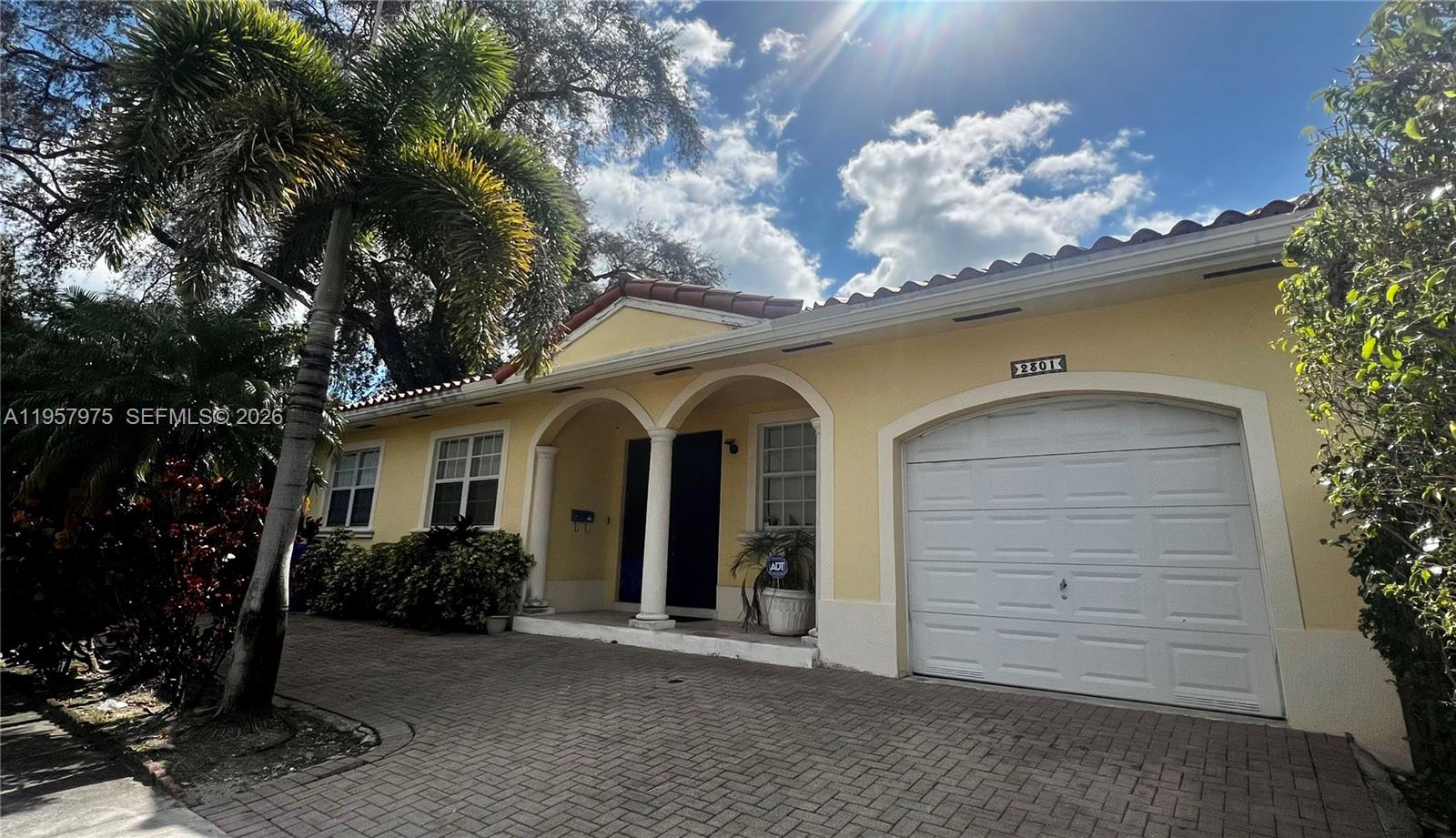 A yellow single-story house features a tiled roof, arched entryway, and a white garage door — 2301 SW 22nd Ave, Miami FL 33145, MIAMI, FL