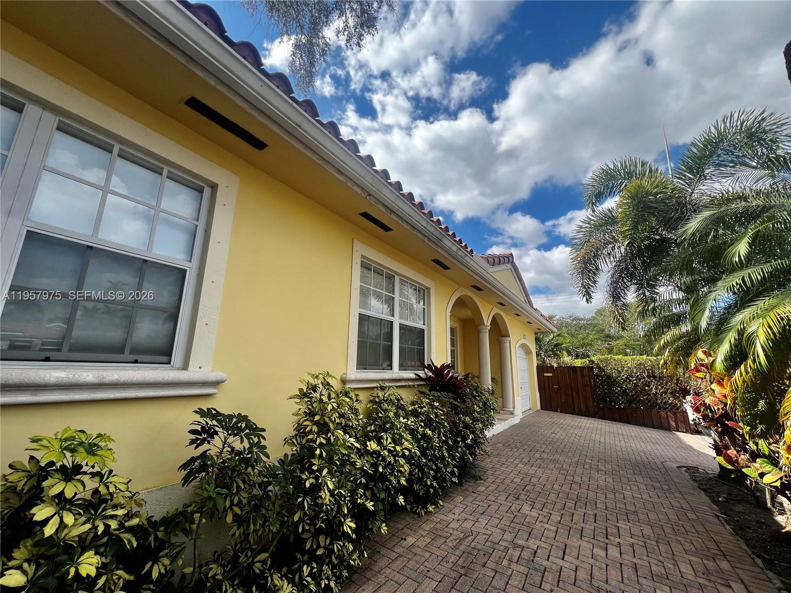 A yellow house with a tiled roof, arched entryway, and brick driveway under a cloudy sky — 2301 SW 22nd Ave, Miami FL 33145, MIAMI, FL