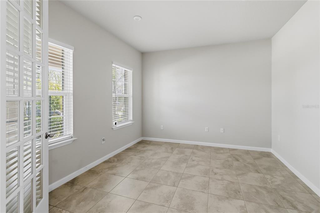 An empty room features light-colored walls, tile flooring, two windows, and white French doors — 5581 VIGO LOOP, ST CLOUD, FL