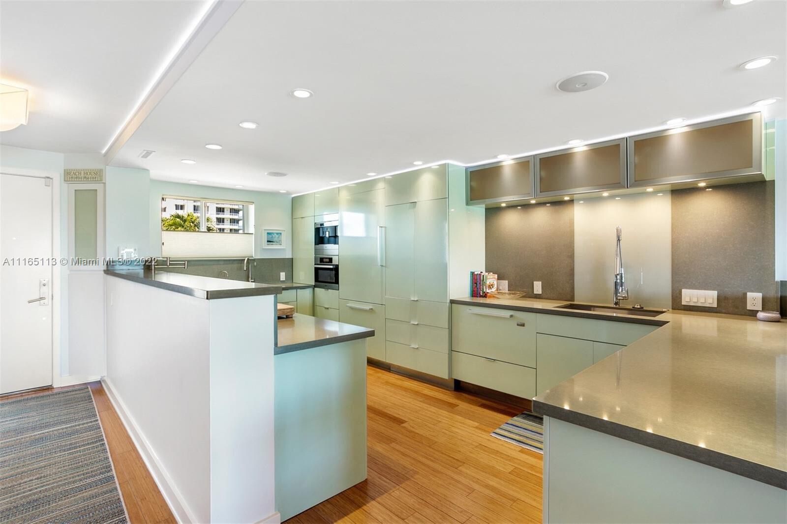 A modern kitchen features light green cabinetry, stainless steel appliances, and wood flooring — 350 S Beach Road # 205, Jupiter FL 33469, JUPITER, FL
