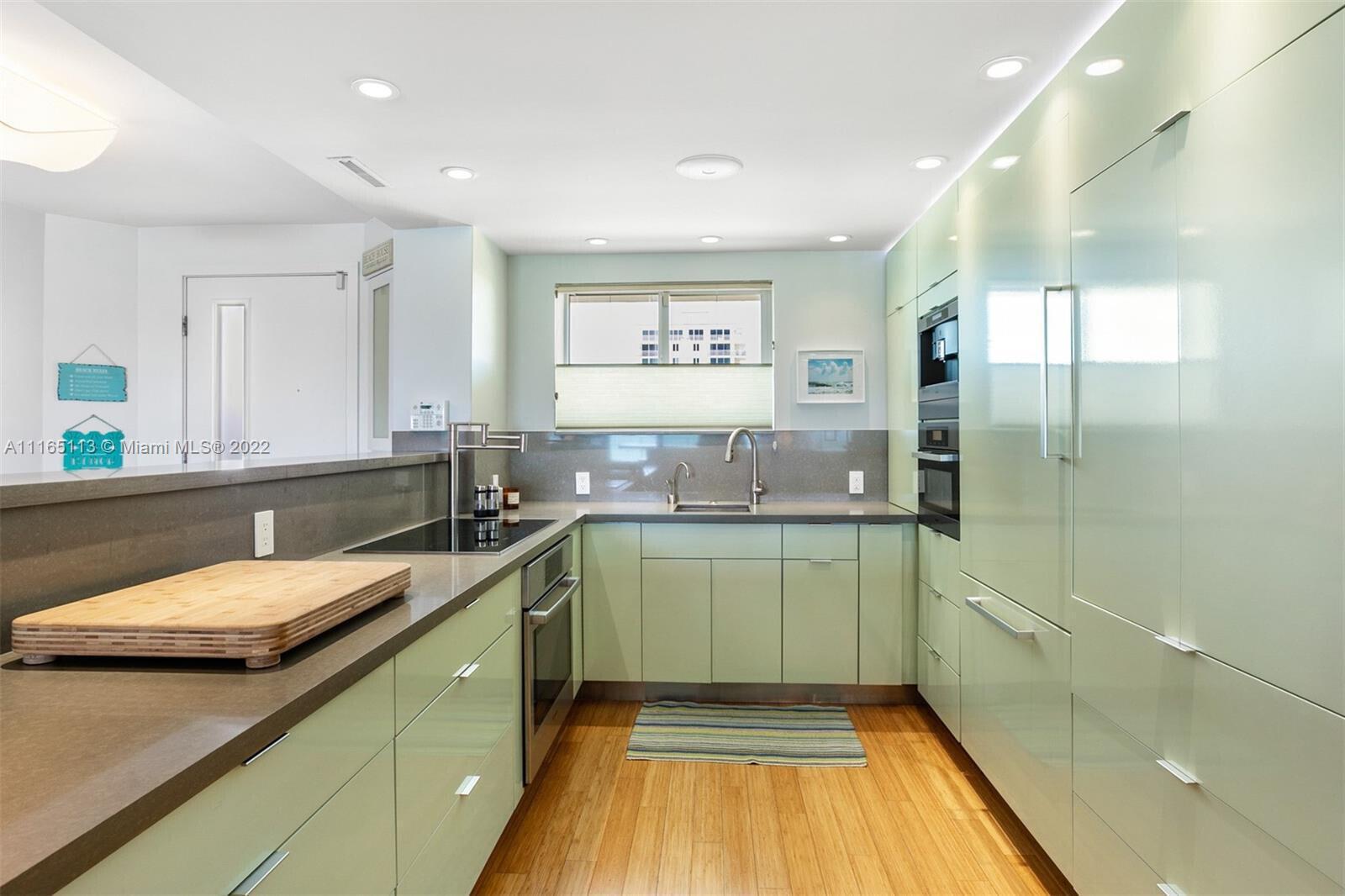 A kitchen features light green cabinetry, dark countertops, stainless steel appliances, and wood flooring — 350 S Beach Road # 205, Jupiter FL 33469, JUPITER, FL