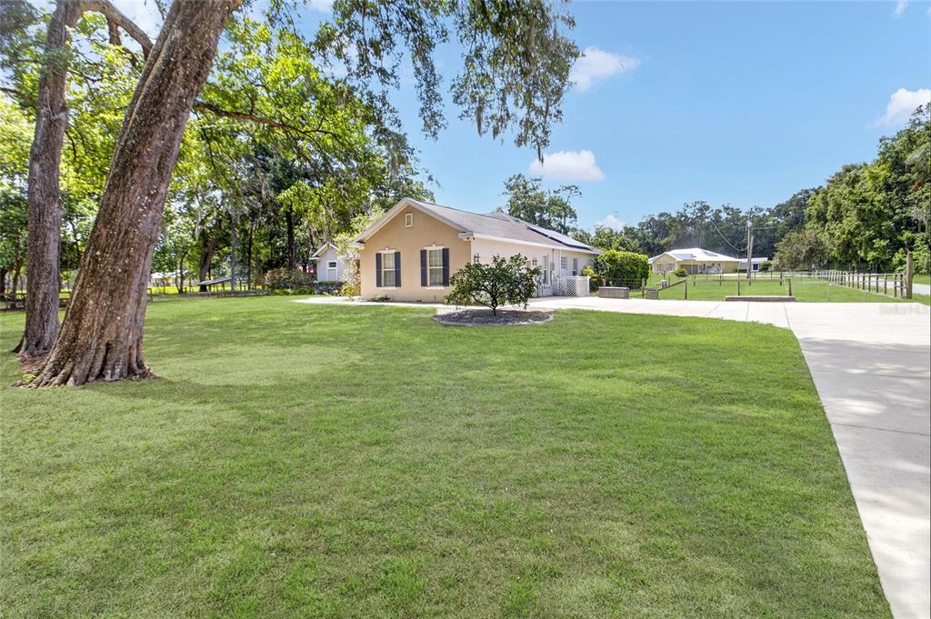 A tan house with dark shutters sits on a large, grassy lot with mature trees — 150 NE 49TH STREET, OCALA, FL