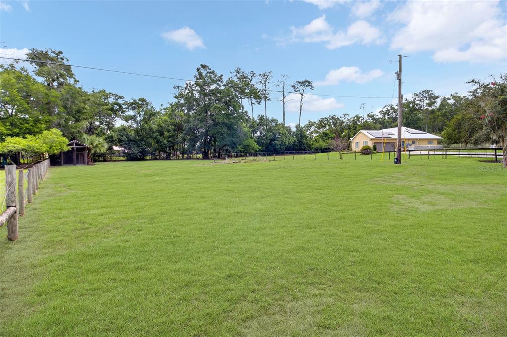 A large, grassy fenced lot with trees and a house in the background — 150 NE 49TH STREET, OCALA, FL