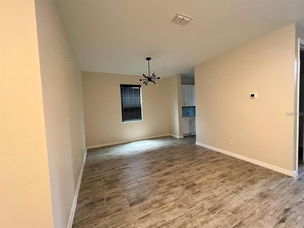 An open-concept dining area features wood-look tile flooring, a modern chandelier, and a window — 700 SPLIT HOOF DRIVE, ST CLOUD, FL