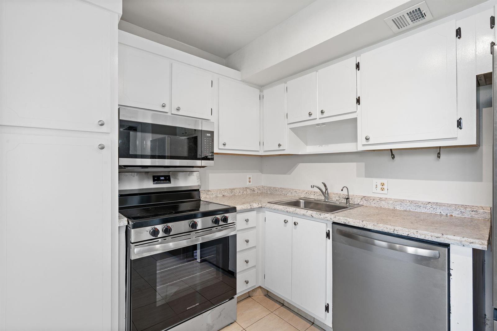 A kitchen features white cabinets, stainless steel appliances, and speckled granite countertops — 2650 S Course Drive Unit 308, Pompano Beach FL 33069, POMPANO BEACH, FL