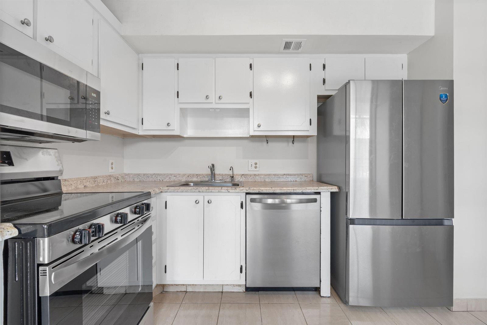 A kitchen features white cabinets, stainless steel appliances, and beige countertops with tiled flooring — 2650 S Course Drive Unit 308, Pompano Beach FL 33069, POMPANO BEACH, FL