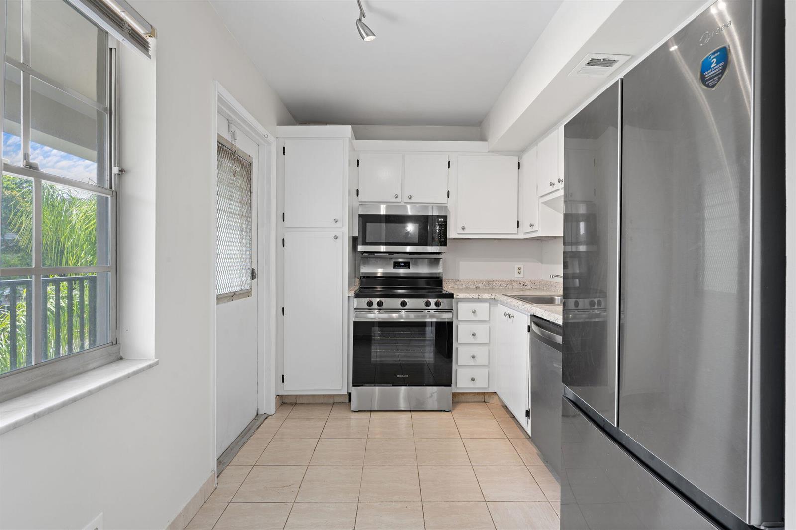 A kitchen features white cabinets, stainless steel appliances, tile flooring, and a window with blinds — 2650 S Course Drive Unit 308, Pompano Beach FL 33069, POMPANO BEACH, FL